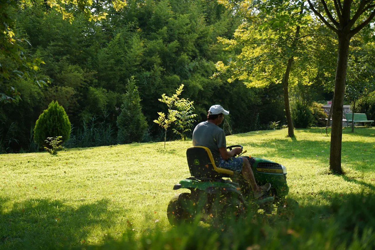 A worker operating a riding lawn mower on green grounds. Illustrative stock photograph.